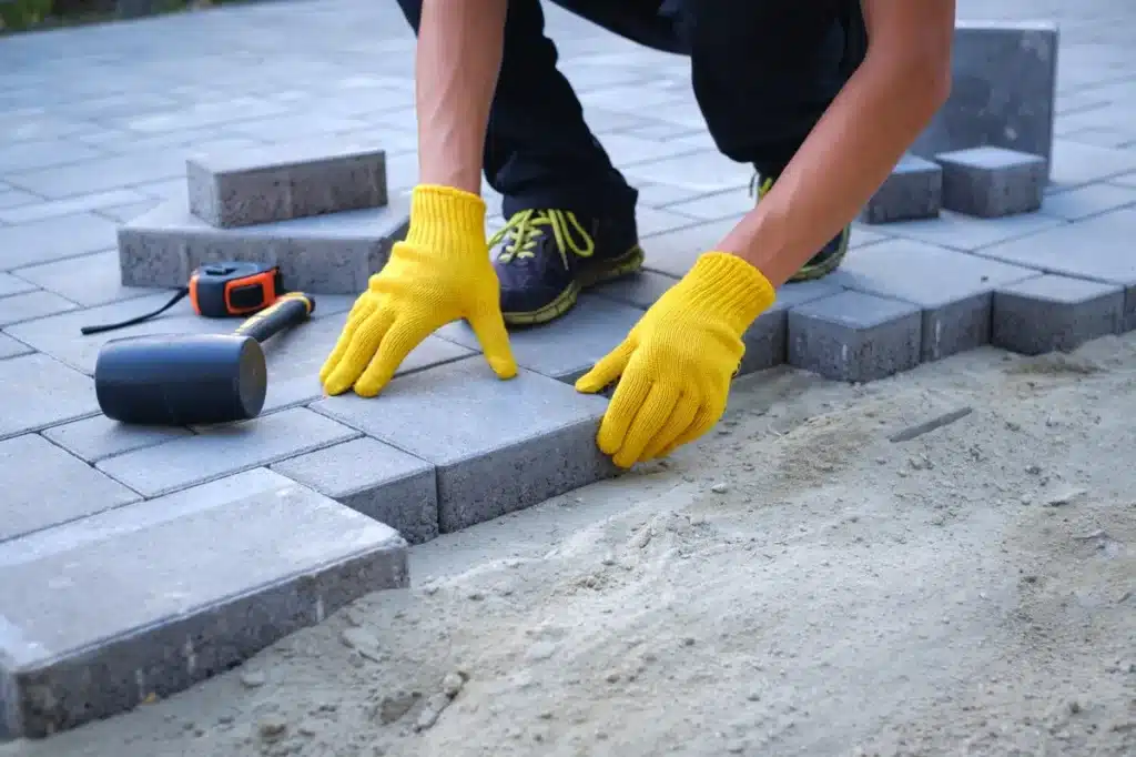 ose de pavés par un ouvrier portant des gants jaunes lors d’un aménagement extérieur